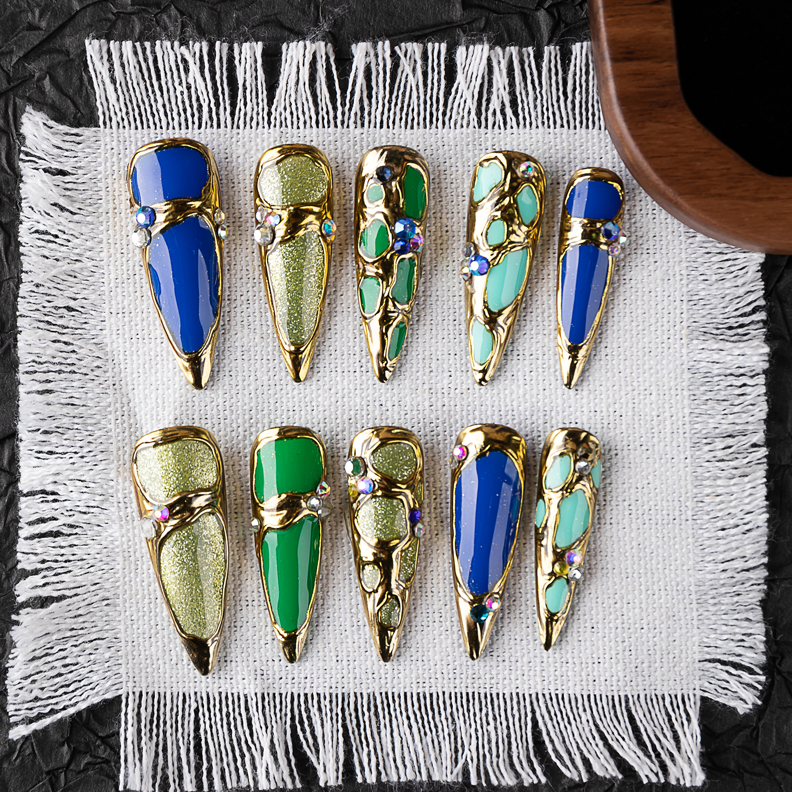 Glossy handmade press-on nails with bold gold 3D metal details, including blue, green and turquoise color combinations. Long stiletto shape, suitable for fashion-forward nail lovers.
